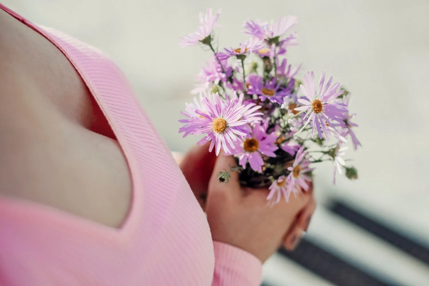 A woman in soft pink holding a small bunch of flowers, representing women's health and wellness